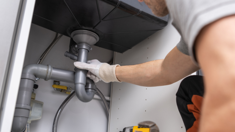 Drain maintenance service in Brighton, Victoria, with a plumber inspecting and repairing the pipework beneath a residential kitchen sink.