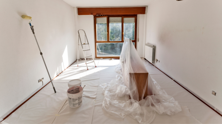 Newly painted living room in Hawthorn, VIC, with fresh white walls, protective floor coverings, paint supplies and a ladder beside a large wooden-framed window.