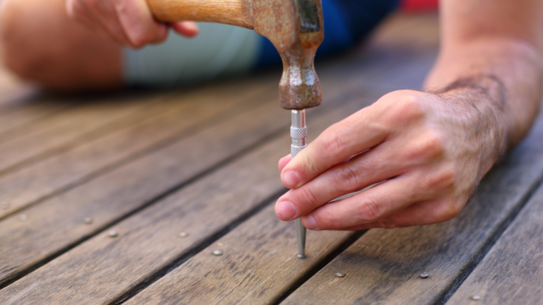 Carpentry service in Port Melbourne, Victoria, with a tradesperson securing timber decking boards using a hammer and nail punch.